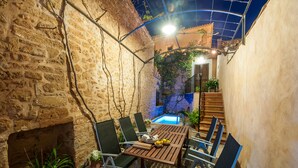 A patio with a wooden table and chairs, a brick wall, and a pool in the background. - Ca Na Blanca (Alcúdia)