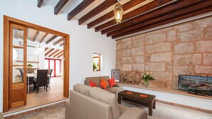 A living room with a stone wall, wooden beams, a sofa, a coffee table, and a television. - Ca Na Blanca (Alcúdia)