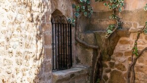 A stone pool with a metal ladder, surrounded by a rustic stone wall with a small window and a metal gate. - Ca Na Blanca (Alcúdia)