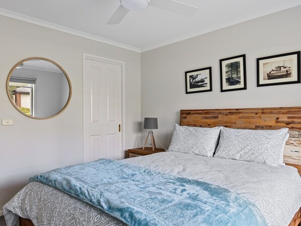 A bedroom with a bed, a round mirror, a door, and three framed pictures on the wall. - Seaside Escape Cowes, Seagrove Wetlands, close to boat ramp and beach. (Cowes)