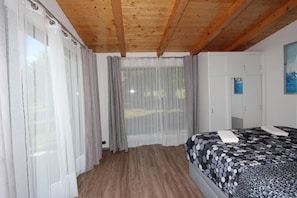 A bedroom with a wooden ceiling, a bed with a patterned bedspread, and a window with sheer curtains. - Holiday House Cuvi (Rovinj)