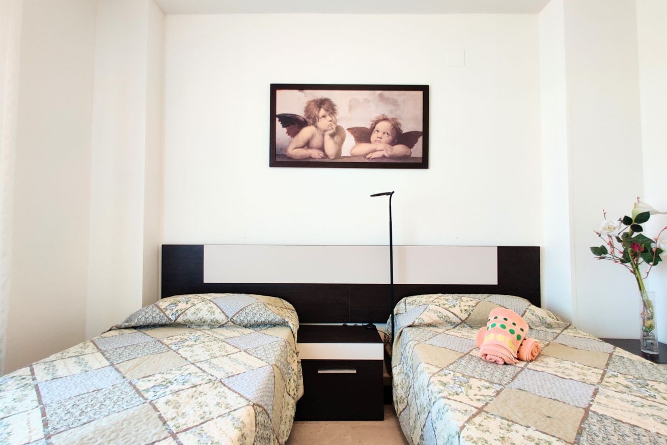 A bedroom with two beds, a black headboard, a framed picture on the wall, and a small plant on the nightstand.