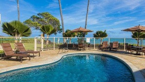 A swimming pool with lounge chairs and umbrellas, surrounded by palm trees and a clear blue sky. - Enjoy A/C, walk to beach/dining/shopping, from the Heart of Kapa'a! (Kapaa)