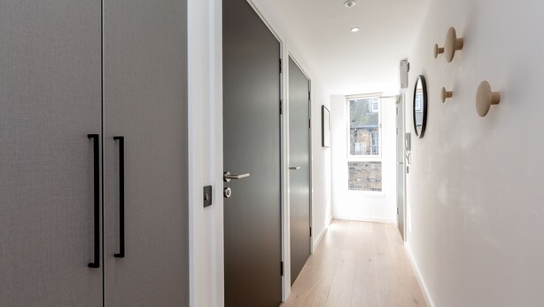 A hallway with a door leading to a balcony, a wall-mounted mirror, and a light fixture. - Destiny Scotland Market St Apartments (Edinburgh)