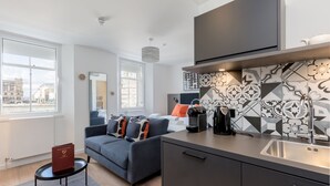 A modern apartment with a kitchen, a dining area, and a living room. There is a large window providing a view of the city. - Destiny Scotland Market St Apartments (Edinburgh)