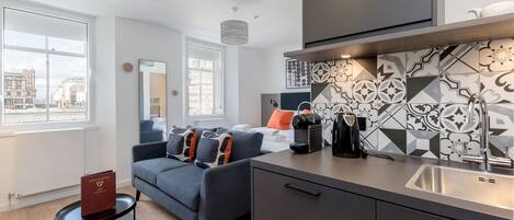 A modern apartment with a kitchen, a dining area, and a living room. There is a large window providing a view of the city.