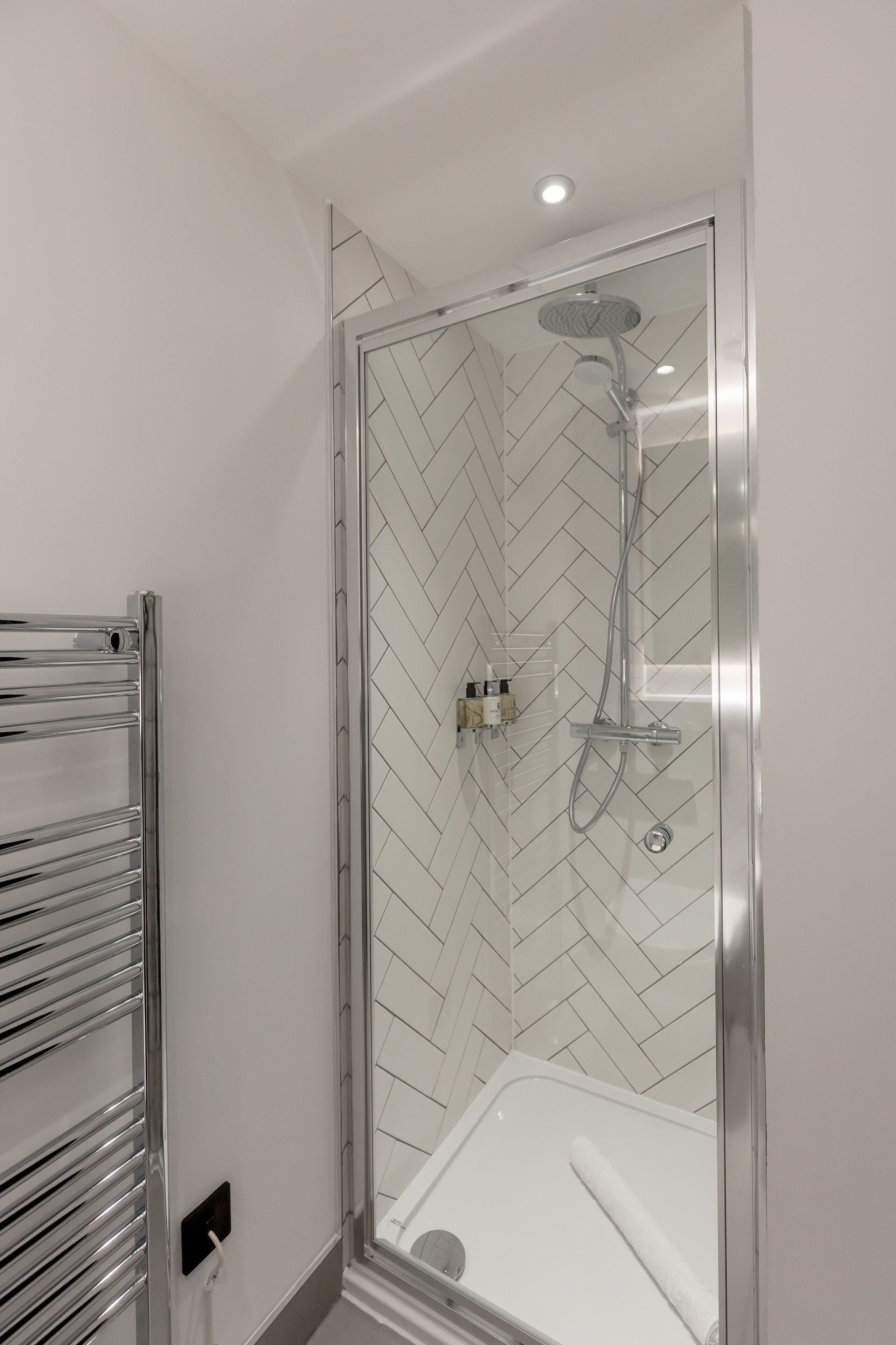 Een moderne douche met glazen cabine, een witte backsplash van visgraat tegels en een chromen handdoekhouder.