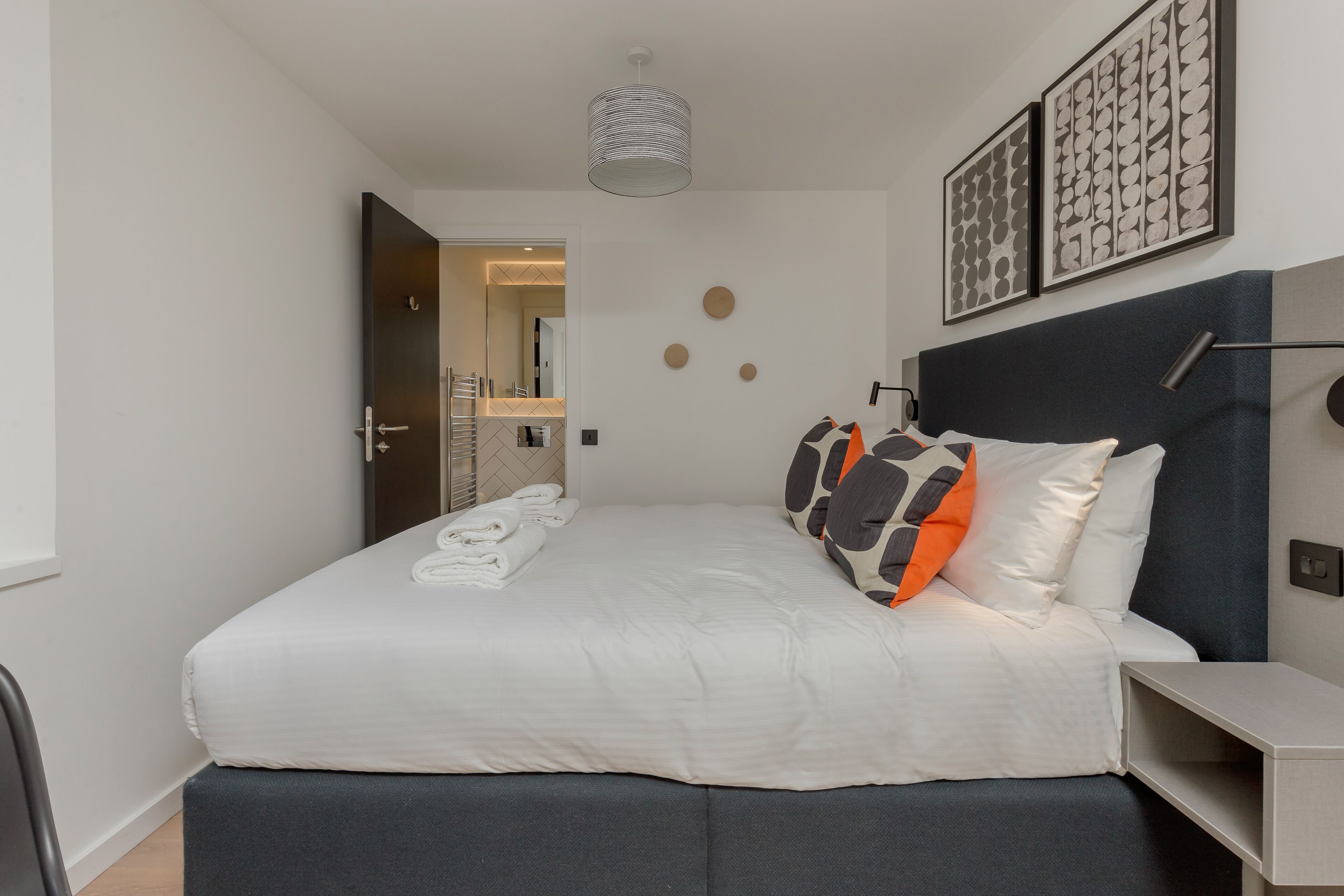 Et moderne hotelværelse med en pænt redt seng, et natbord og en sengegavl.