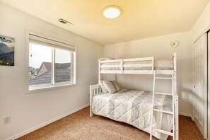 A room with a bunk bed, a window with a view of houses, and a door.
