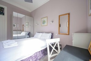 Una camera da letto con un letto, una sedia, una scrivania, uno specchio e un armadio.