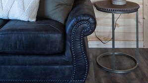 Ein Zimmer mit einem dunkelbraunen Ledersofa, einer weißen Strickdecke, einer Metalllampe auf einem kleinen Tisch und Holzpaneelen an den Wänden.