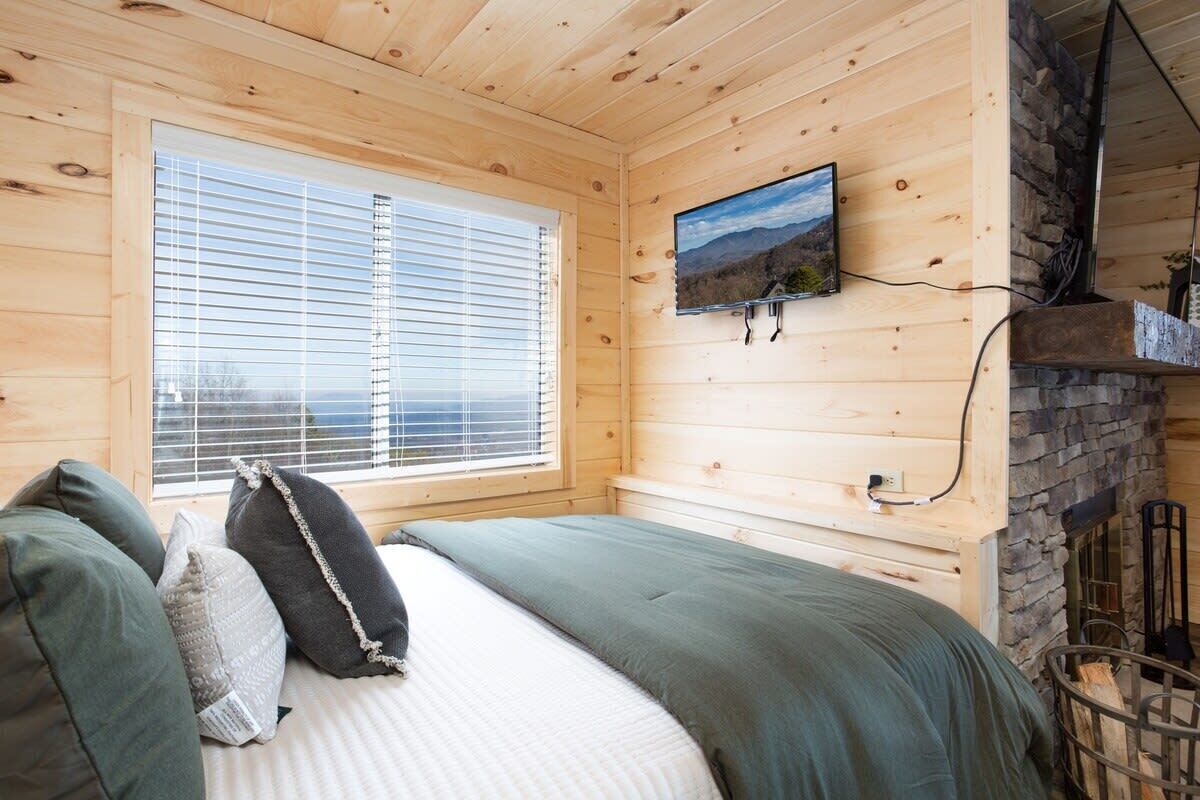 Una habitación con paneles de madera, una cama, un televisor montado y una chimenea de piedra.