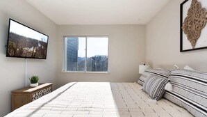 Ein Schlafzimmer mit einem großen Bett, einem Wandfernseher, einem Fenster mit Ausblick und einem dekorativen Wandbild.