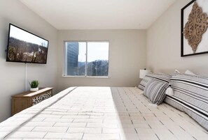 Ein Schlafzimmer mit einem großen Bett, einem an der Wand montierten Fernseher, einem Fenster und einer Wanddekoration.