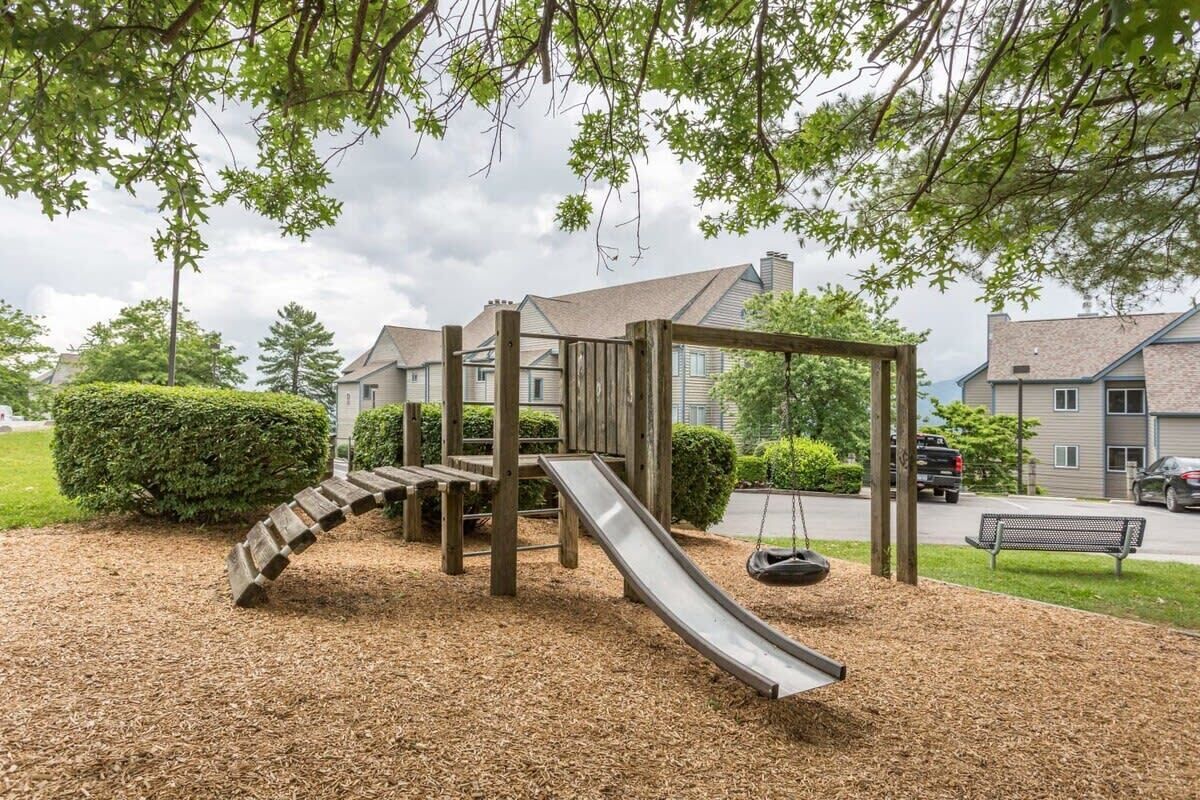 A playground with a slide and swing set, surrounded by mulch and trees.