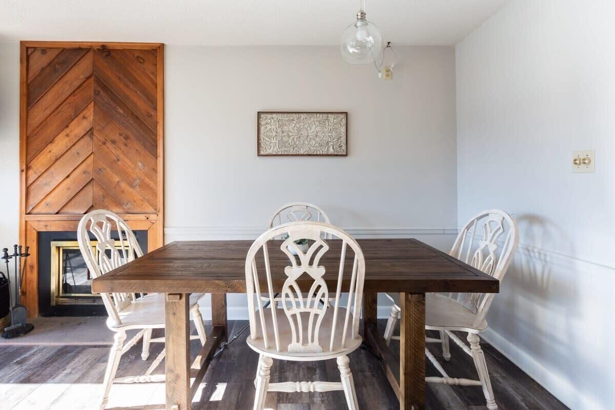A dining area with a wooden table and white chairs, a decorative wall piece, and a fireplace.