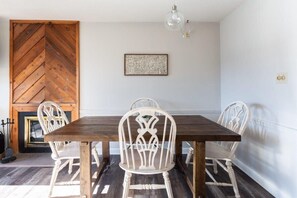 Un área de comedor con una mesa de madera y sillas blancas, un adorno en la pared y una chimenea.