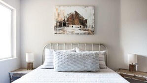 Une chambre à coucher avec un lit, des oreillers, un tableau accroché au mur, des lampes de chevet et une fenêtre.