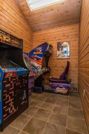 A small room with wooden walls and a tiled floor, containing a vintage arcade machine and a purple gaming console. - Awesome Views Of GSMNP/Indoor Pool & Hot Tub (Gatlinburg)