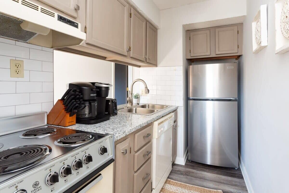 A compact kitchen with a built-in oven, a stainless steel refrigerator, and a coffee maker.
