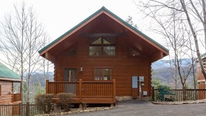 Une cabane en bois avec un toit à deux versants, une véranda à l’avant et une vue sur les montagnes en arrière-plan.