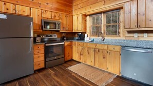 Une cuisine de style rustique, avec des meubles en bois, un réfrigérateur, un four à micro-ondes, une cuisinière et un lave-vaisselle.