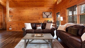 Un intérieur de chalet chaleureux avec un plafond en bois, un canapé en cuir marron, une table basse en bois et une décoration murale représentant un cerf.