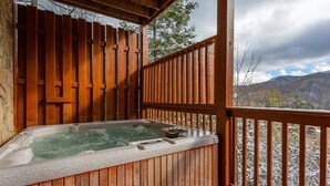 Una bañera de madera caliente en un balcón con vistas a montañas nevadas.