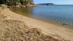 Een strand met helder water, een zandstrand en bomen op de achtergrond.