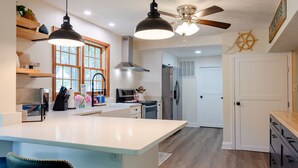 Een moderne keuken met een centraal eiland, hanglampen, een plafondventilator en uitzicht op de eethoek.