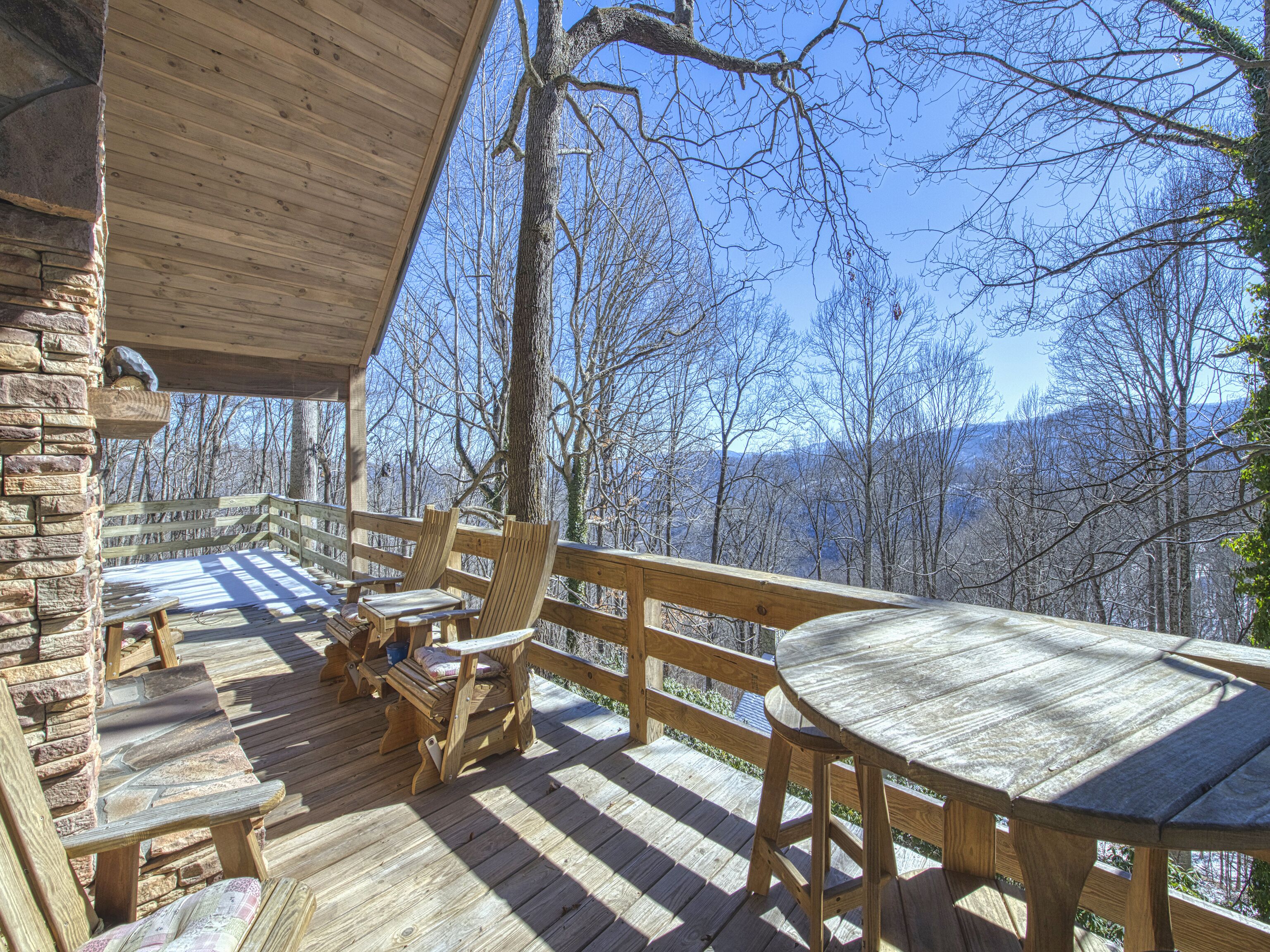 A wooden deck with benches and a table, overlooking a forested area.