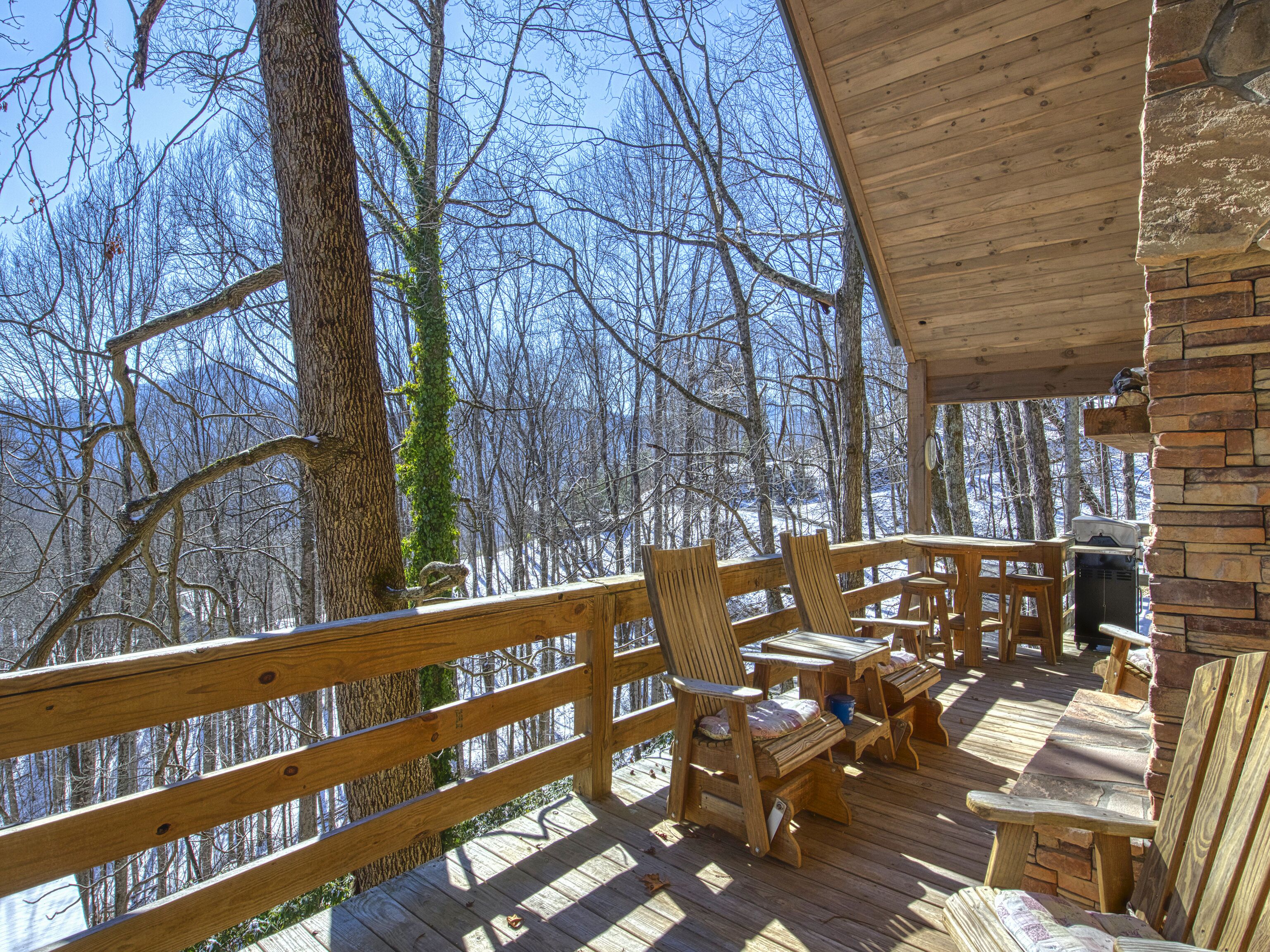 A wooden deck with outdoor seating, surrounded by trees and a mountainous backdrop.