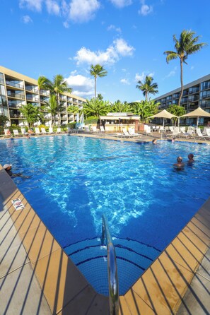Une piscine à l’eau d’un bleu cristallin, entourée de chaises longues et de palmiers.
