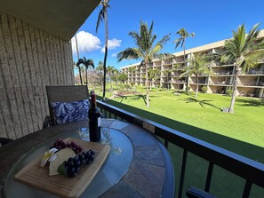 Un balcon avec une table dressée pour un repas, donnant sur une pelouse bien entretenue et un immeuble doté de nombreux balcons.
