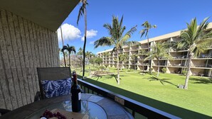A balcony with a table set for a meal, overlooking a well-maintained lawn and a building with multiple balconies. - Where Serenity Finds You Kihei Remodeled 1BR Condo Private Lanai and Pool (Kihei)