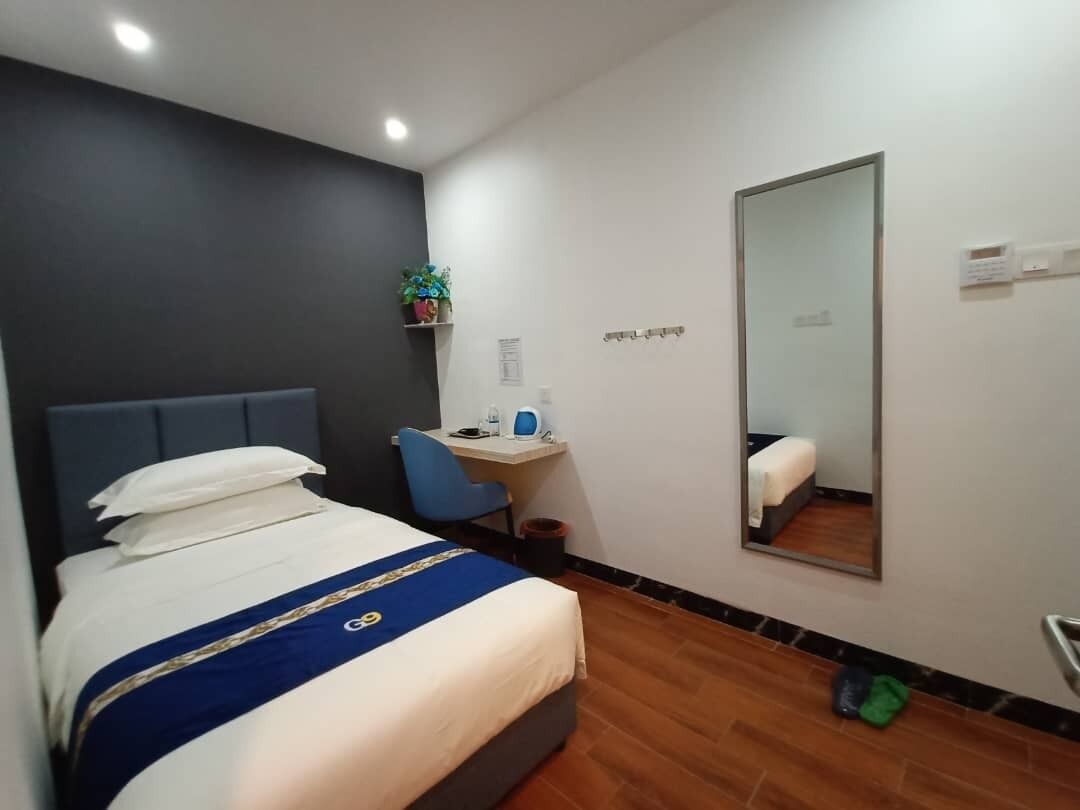 Habitación de hotel con cama, escritorio, silla, espejo y una planta pequeña.