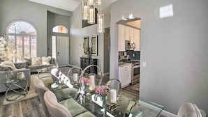 A modern living room with a glass dining table, grey sofas, and a kitchen in the background. - On Golf Course! Snowbird Resort Retreat in Mesa (Mesa)