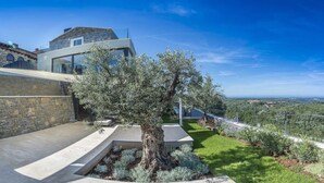 A modern house with a stone facade, a glass conservatory, and a well-maintained garden with a prominent olive tree. - Villa Fortezza - pool, sauna, Jacuzzi and countryside views by MyWaycation (Buje)
