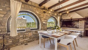 A rustic stone kitchen with a built-in oven, two large arched windows with stained glass, and a dining area with white chairs and a wooden table. - Villa Fortezza - pool, sauna, Jacuzzi and countryside views by MyWaycation (Buje)