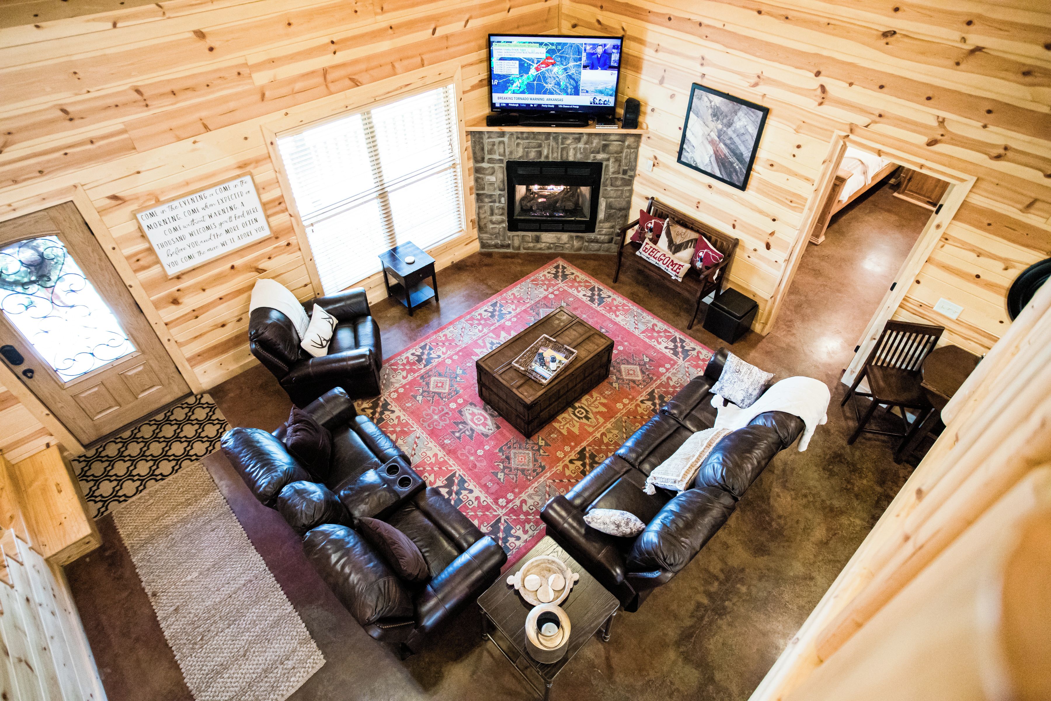 A log cabin interior with a fireplace, leather sofas, a coffee table, and a television.