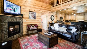 Ein gemütliches Blockhaus-Interieur mit Kamin, Ledersofa und an der Wand befestigtem Fernseher.