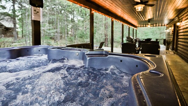 Ein Whirlpool mit Holzterrasse und Lichterkette, umgeben von einem Wald.