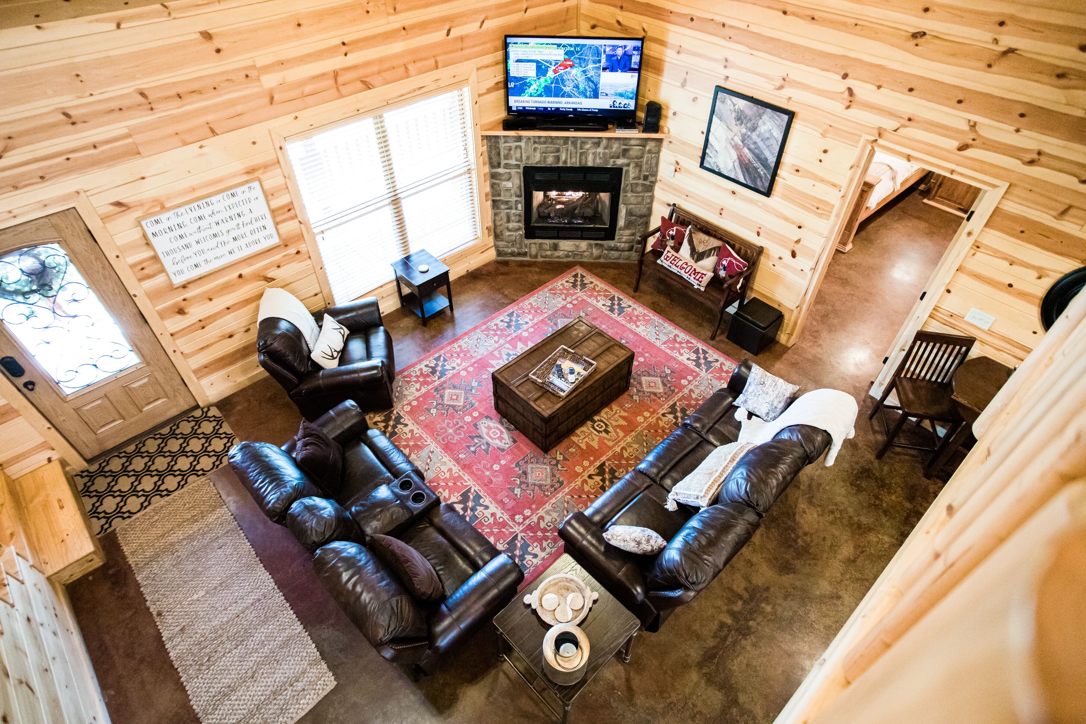 A log cabin interior with a fireplace, leather sofas, a television, and a patterned rug.