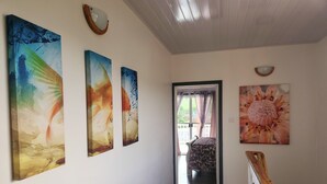 A hallway with wooden flooring, a staircase with a wooden handrail, and three large paintings on the wall. - The Best of Home - Tranquil, Comfort & Convenient (Beausejour)