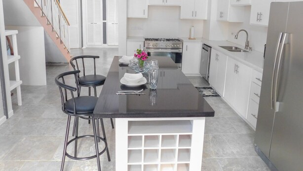 A modern kitchen with white cabinets, a central island with stools, a stainless steel refrigerator, and a gas stove. - The Best of Home - Tranquil, Comfort & Convenient (Beausejour)