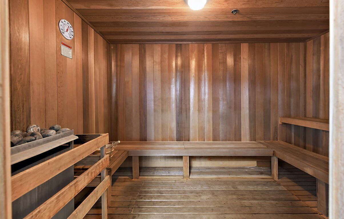 A sauna with wooden walls and benches, a clock, and a heater on the left.