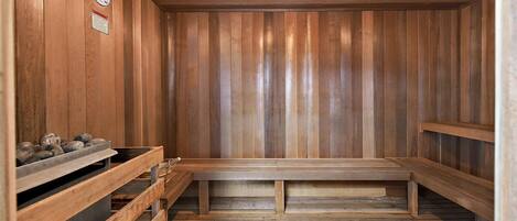 A sauna with wooden walls and benches, a clock, and a heater on the left.