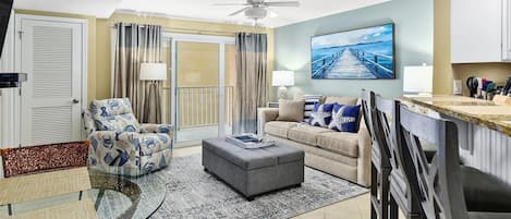 Una sala de estar con sofá, sillón, reposapiés y una mesa de centro de vidrio.