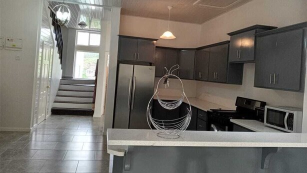 Une cuisine moderne avec des meubles de couleur sombre, un plan de travail blanc et un luminaire suspendu.