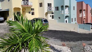A multi-story residential building with balconies, a parking area, and a palm plant in the foreground. - The Best of Home - Tranquil, Comfort & Convenient (Beausejour)